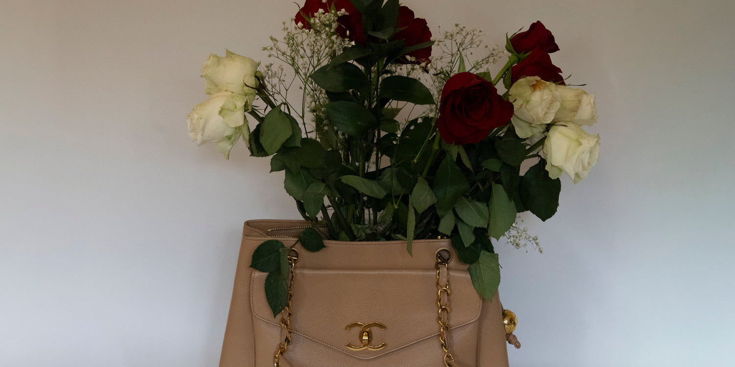 A beige Chanel handbag filled with red and white roses and greenery against a plain background.