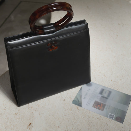 Black handbag with tortoiseshell handle on a light surface