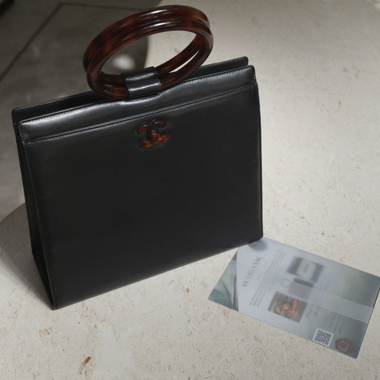 Black handbag with tortoiseshell handle on a light surface