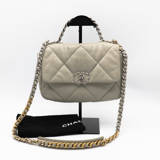 Quilted handbag with chain strap on a stand, accompanied by a black pouch with 'Chanel' branding.