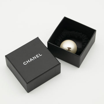 A Chanel-branded black box with a removable lid, containing a hair scrunchie adorned with a faux pearl with a 'CC' Chanel logo.