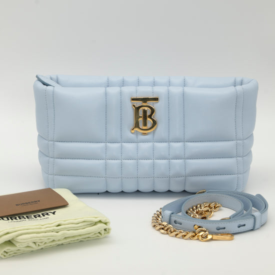 Light blue quilted Burberry handbag with gold 'TB' logo, chain strap, and Burberry dust bag on a white background
