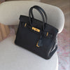Black handbag with gold hardware on a light gray chair