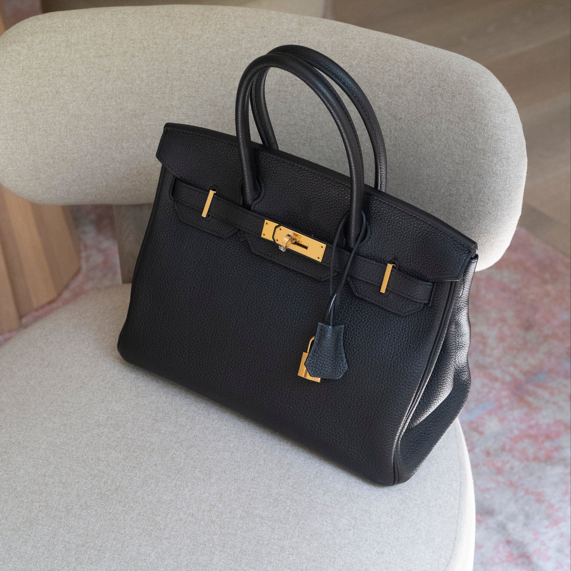 Black handbag with gold hardware on a light gray chair