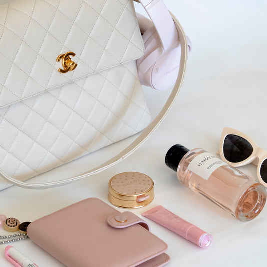 White quilted handbag with Chanel logo, sunglasses, lip gloss, and perfume bottle on a white surface