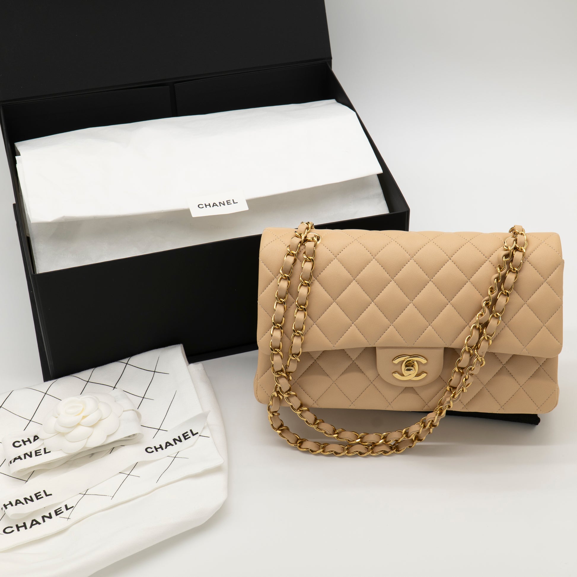 Beige quilted handbag with gold chain and Chanel logo next to a black Chanel box on a white background.