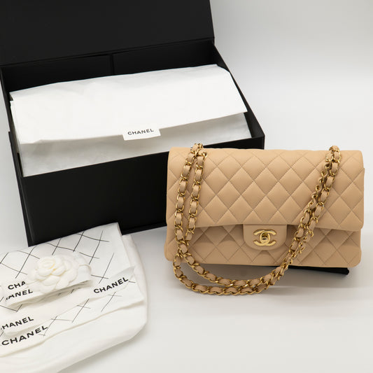 Beige quilted handbag with gold chain and Chanel logo next to a black Chanel box on a white background.